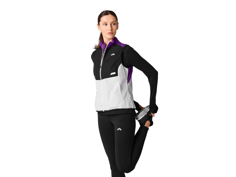 Woman stretching, wearing a black and white sports vest, long-sleeved top, and black leggings.