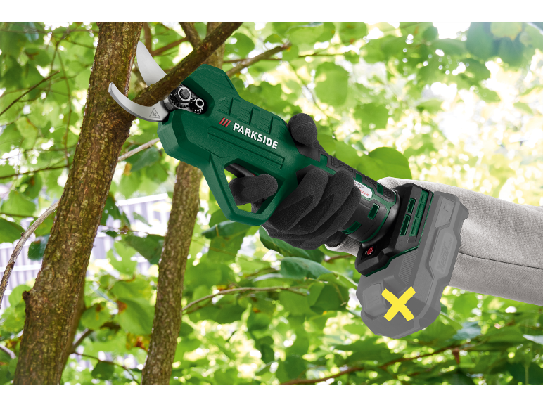 Person in gloves uses cordless pruning shears to trim a tree branch.