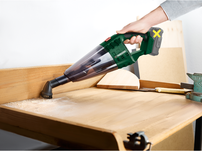 Handheld vacuum cleaner clearing wood shavings from a workbench.