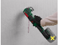 Cordless multi-tool with a grout accessory, being used on a wall.