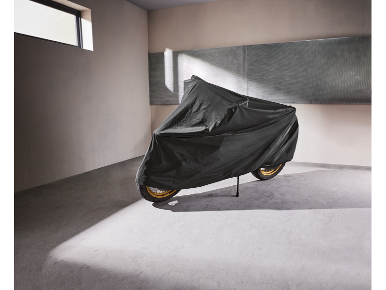 Motorcycle covered with a protective tarp in a garage with sunlight.
