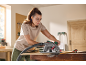 Woman cutting wood with a circular saw in a workshop, wearing safety glasses and earplugs.