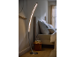 Curved LED floor lamp in a modern bedroom with a bed and nightstand.