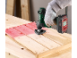 Cordless multi-tool sanding a red wooden surface on a workbench.