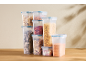 Clear storage containers with pasta, cereal, dried fruit, and nuts on a wooden table.