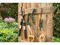 Garden shears, saws, and pruners hang on a wooden wall in front of a garden.