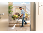 Man cleaning a patio with a pressure washer, with potted plants in the background.