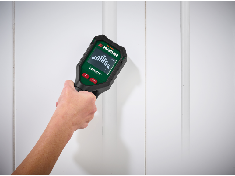 Hand holding a digital wall scanner against a white wall, displaying a signal.