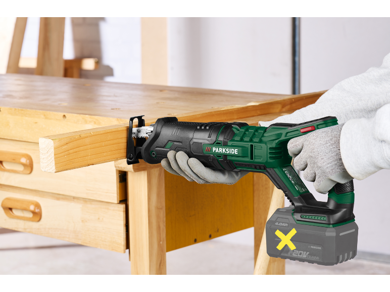 Cordless reciprocating saw cutting a wooden plank on a workbench.