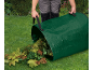 Person emptying leaves from a green garden bag onto the grass.