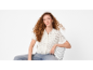 Woman with curly hair, white knitted shirt and jeans, sitting on a chair.