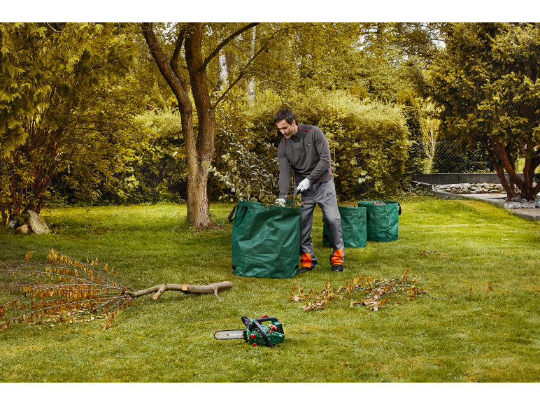 Man filling garden bags with cut branches, chainsaw on the ground.