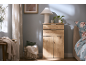 Wooden cabinet with drawers and doors, table lamp, plant, and basket with blanket in a bedroom.