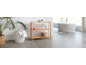 Modern bathroom with a wooden shelving unit, laundry basket, and white bathtub.