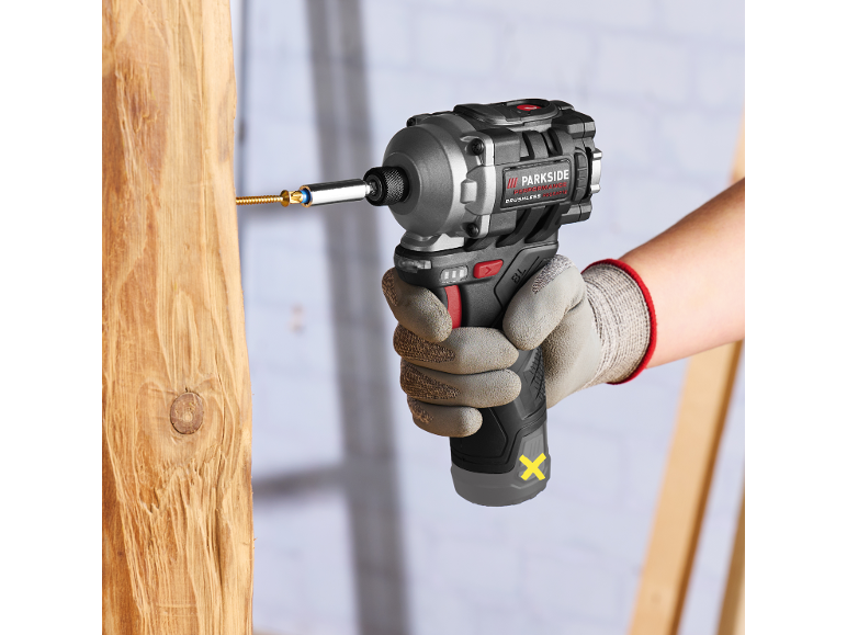 Gloved worker using a cordless impact driver to screw a screw into wood.