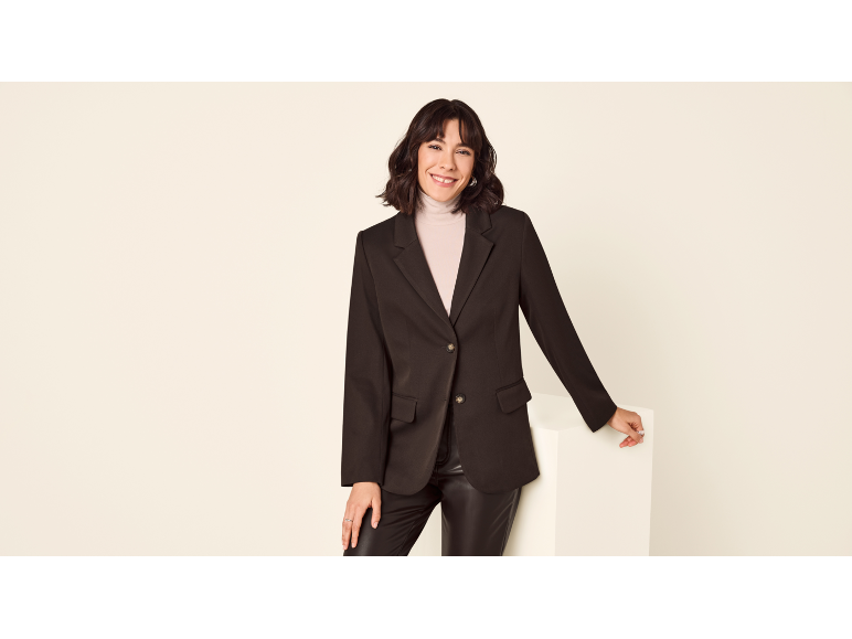 Woman in a black blazer, faux leather trousers, and a beige turtleneck, smiling.