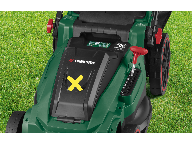 Green lawnmower with a yellow 'X' symbol and height adjustment lever on green grass.