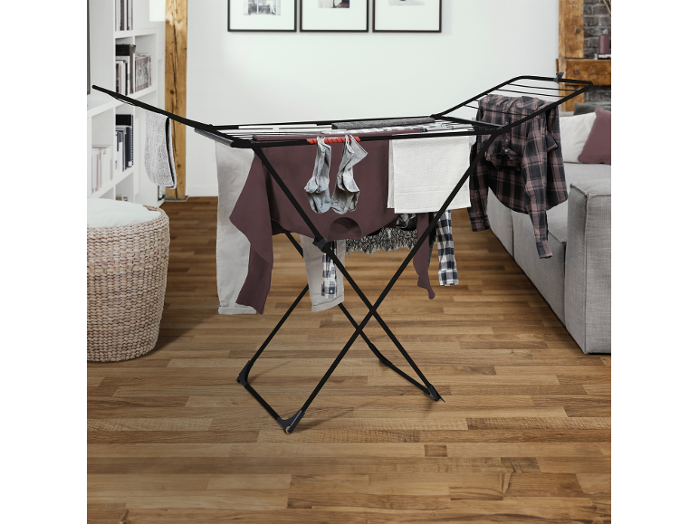 Black clothes drying rack with various clothes in a modern living room.
