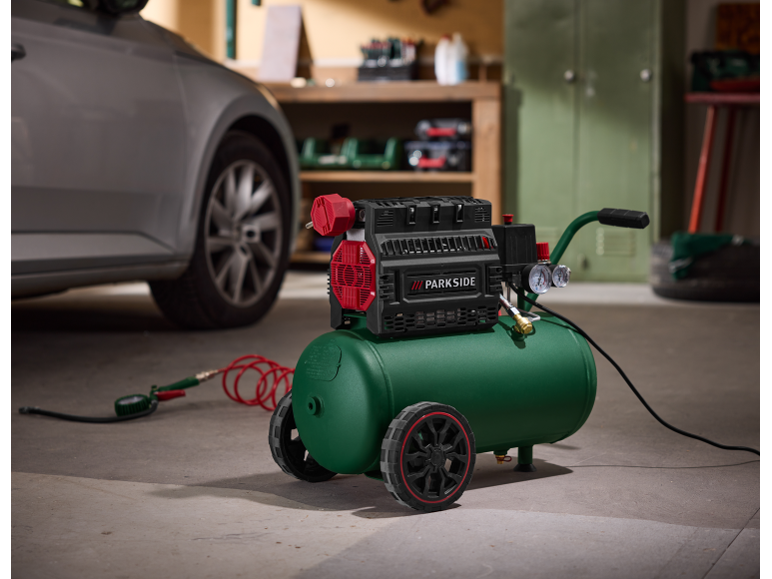 Green and black air compressor with wheels in a garage with a car.