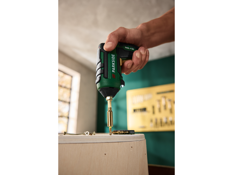 Hand holding a green cordless screwdriver with a bit, ready to screw into wood.
