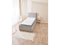 Single bed with grey upholstered frame, white mattress, and a cream rug on a wooden floor.