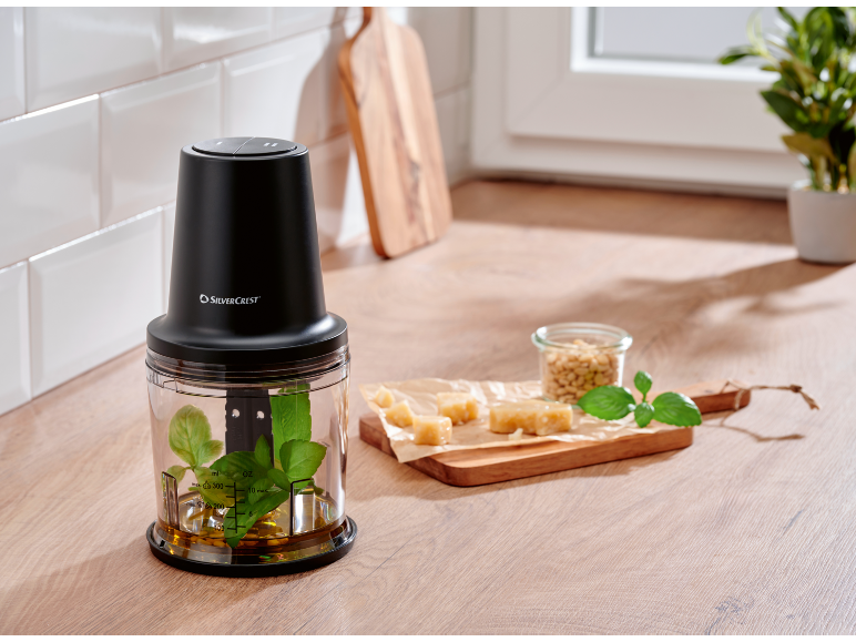 Black food chopper with pesto ingredients on a kitchen counter.