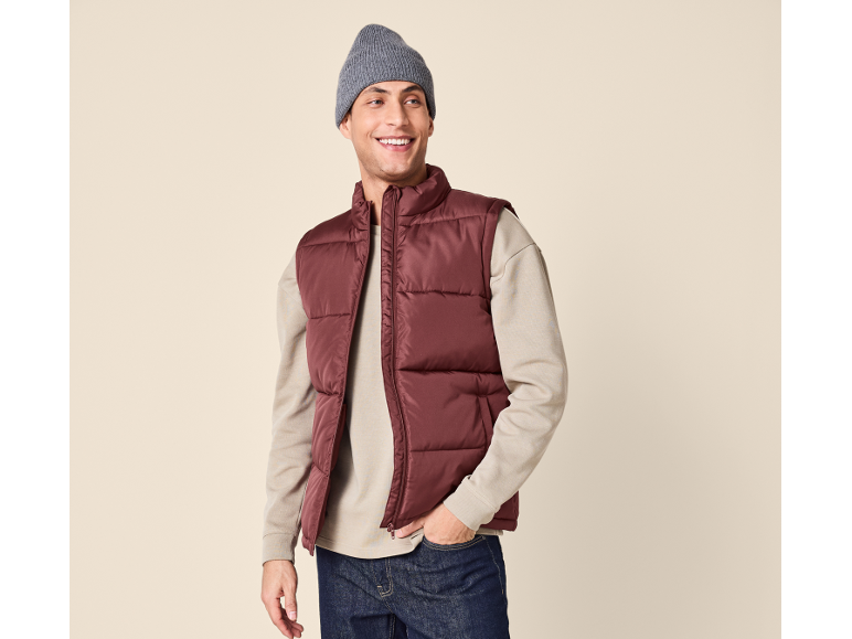 Smiling man wearing a burgundy puffer vest, beige sweater, and grey beanie.