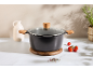Black pot with wooden handles and glass lid on a wooden trivet.