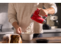 Man whisking cream with a red hand mixer, with a cake beside it.