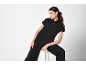 Woman in black short-sleeved jumpsuit with wide-leg trousers, with gold earrings and arm cuff.