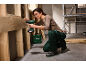 Woman in safety glasses using a cordless drill on a wooden construction.
