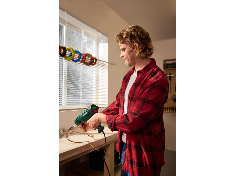 Man in a workshop using a heat gun on electrical wires.