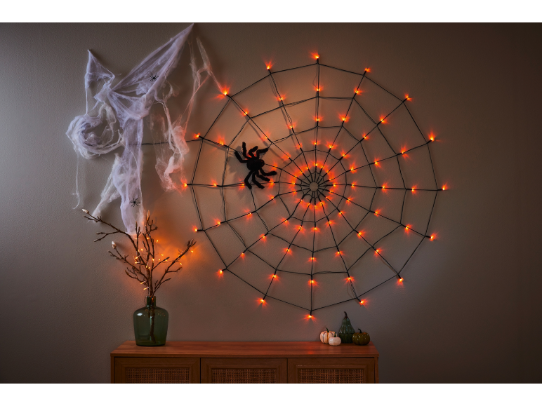 Spiderweb with orange lights, spider, and decorative branches for Halloween.