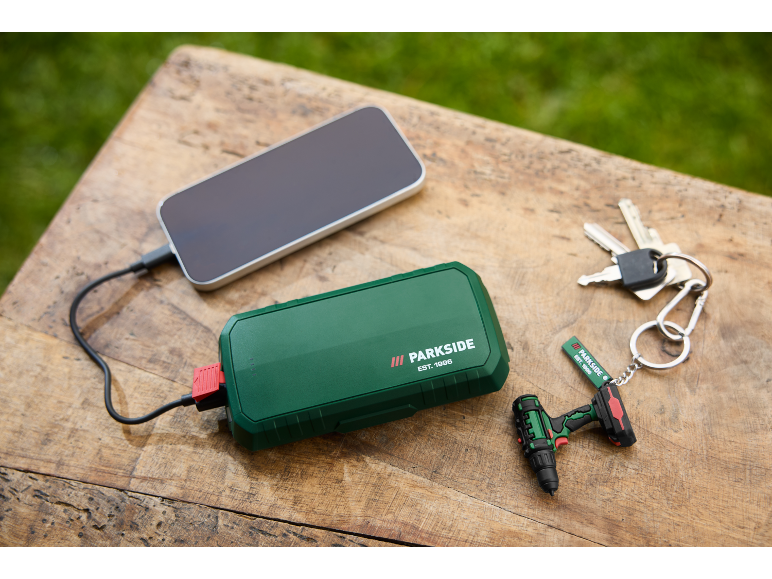 Green power bank charging a smartphone, with keys and a mini drill keychain.