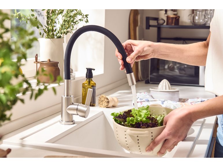 Kitchen faucet with flexible hose rinsing lettuce in a colander over the sink.