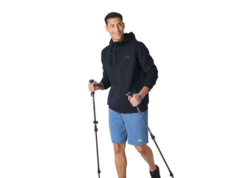 Smiling man in black hoodie, blue shorts, and trekking poles.
