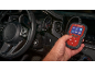 Hand holding a car diagnostic tool with a screen displaying various functions inside a car.