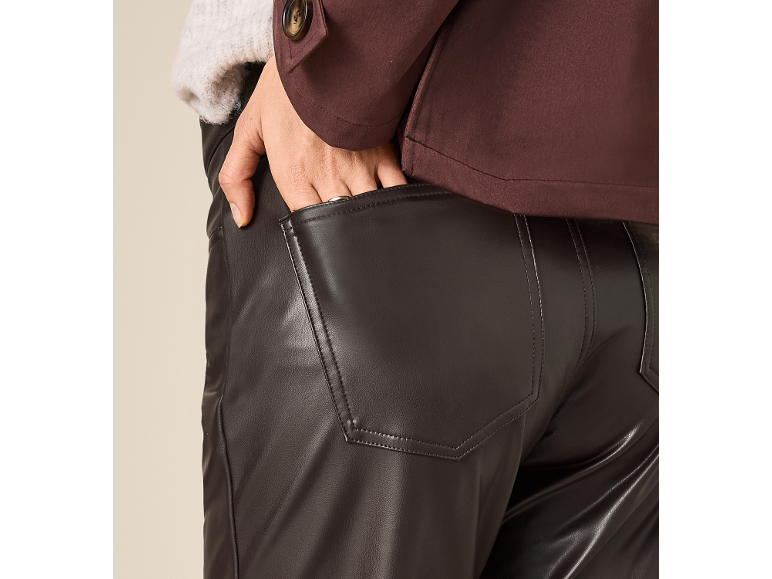 Detail of a woman in brown faux leather trousers and a burgundy jacket.