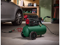 Green and black air compressor with wheels in a garage with a car.
