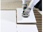 Person using a tile vibrator on white floor tiles with adhesive spread on the floor.