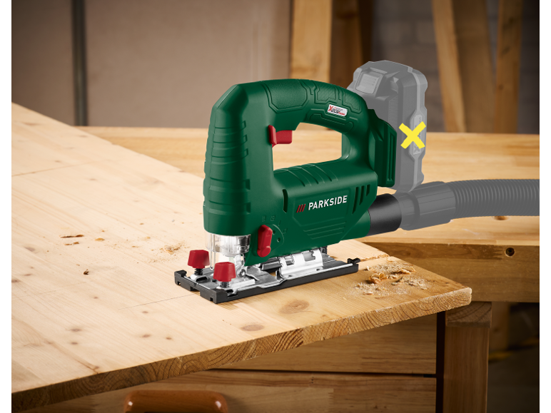 Green jigsaw with battery and suction hose, cutting wood.