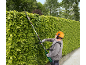 Man trimming a tall hedge with a long-reach hedge trimmer, wearing a safety helmet.