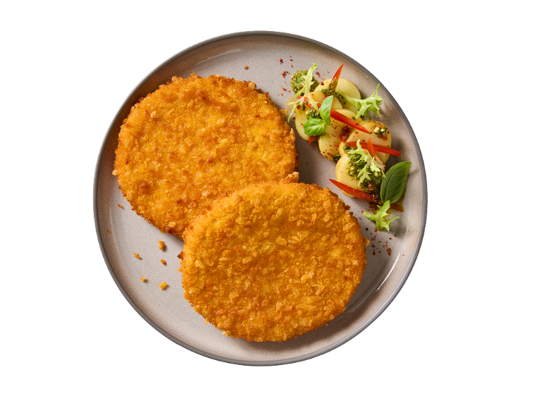 Two breaded cutlets with a side of potatoes, pesto, and red pepper on a plate.