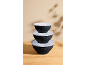Stackable black bowls with white lids on a wooden table.