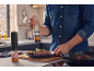 Man seasoning a steak with an electric pepper grinder in a kitchen.