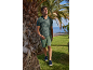 Man in green patterned polo shirt and shorts, walking among palm trees by the sea.