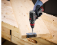 Cordless drill driving a screw into a metal hinge attached to a wooden plank on a workbench.