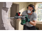 Man with a hammer drill, safety glasses, mask, and ear protection breaking down a wall.