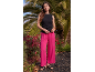 Woman in black top and bright pink wide-leg trousers in front of palm trees.