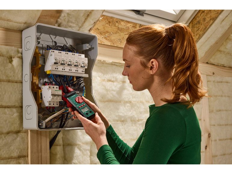 Woman measuring current in a fuse box with a clamp meter.